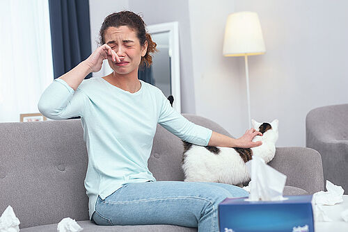 Frau mit Tierhaarallergie sitzt mit Katze auf Sofa